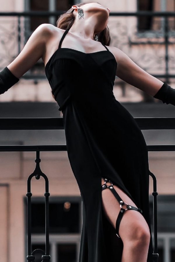 Beautiful young retro woman in a luxurious black glamorous evening dress. Leather fashionable leg straps. Elegant tall gloves. Girl fashion model posing. Threw back head. Vintage buildings background